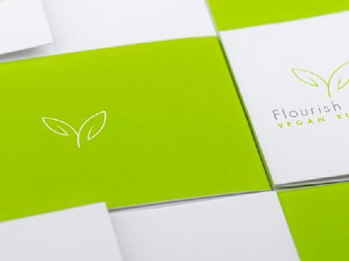 a close up of a green and white business card with a plant logo on it for flourish vegan kitchen.