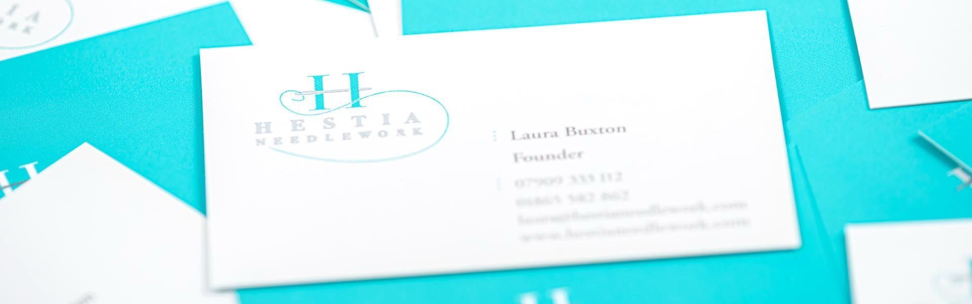 a business card for hestia needlework is on a blue surface