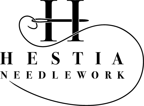 A black and white logo for a company called hestia needlework.