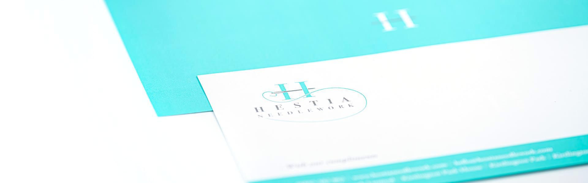 a business card for hestia needlework sits on a table 