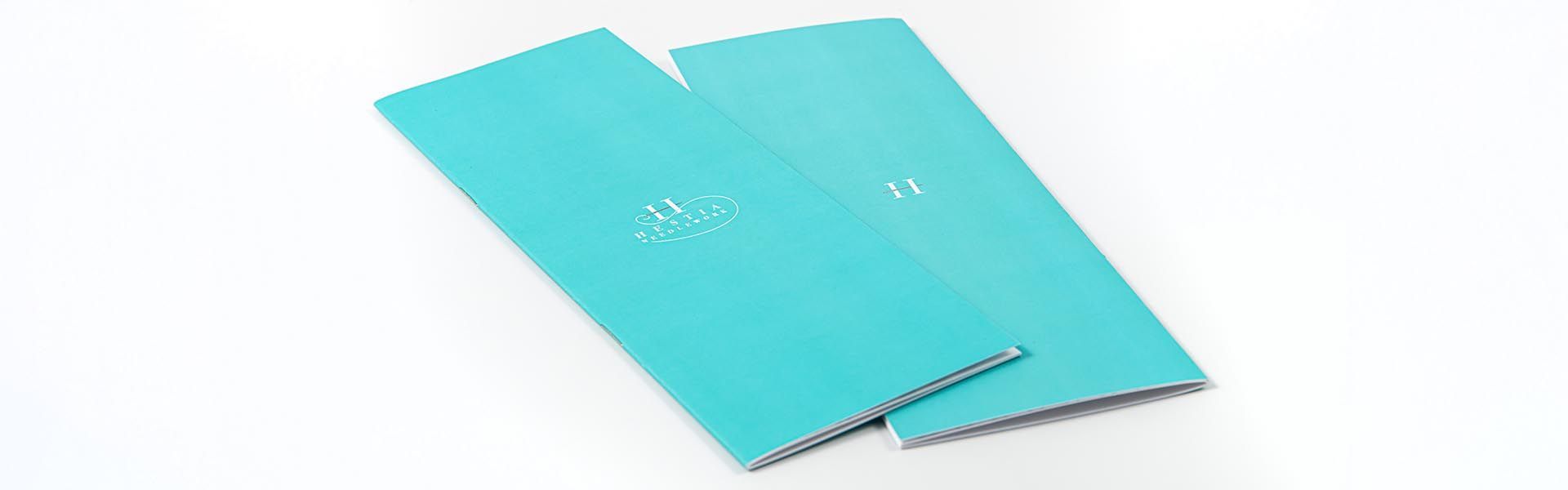 two blue brochures with the hestia needlework logo on them