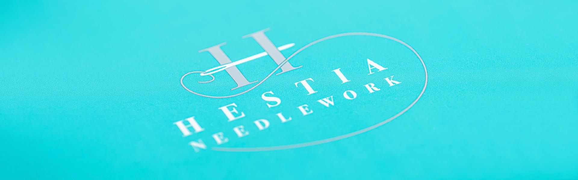 the logo for hestia needlework is on a blue background 