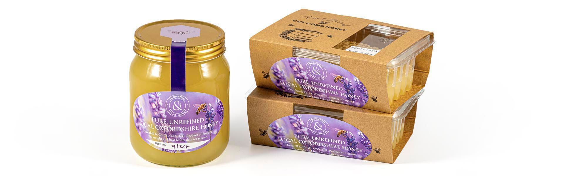 A jar of honey and a two boxes of cut comb honey are stacked on top of each other.