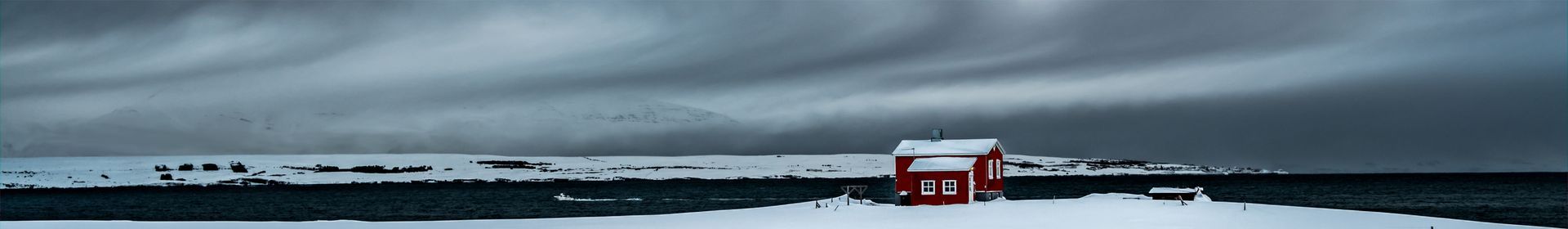 a red house in the middle of a snowy field on a cloudy day .