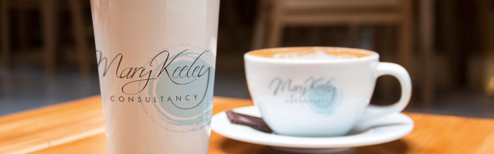 a cup that says mary keeley consultancy sits next to a cup of coffee
