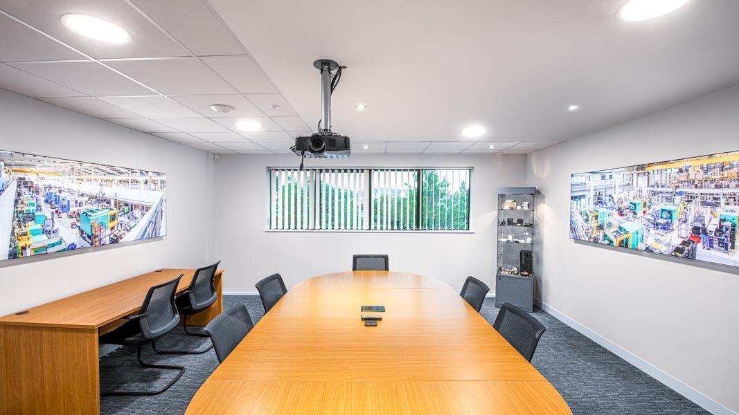 a conference room with two large illuminated factory panorama photographs and a projector on the ceiling