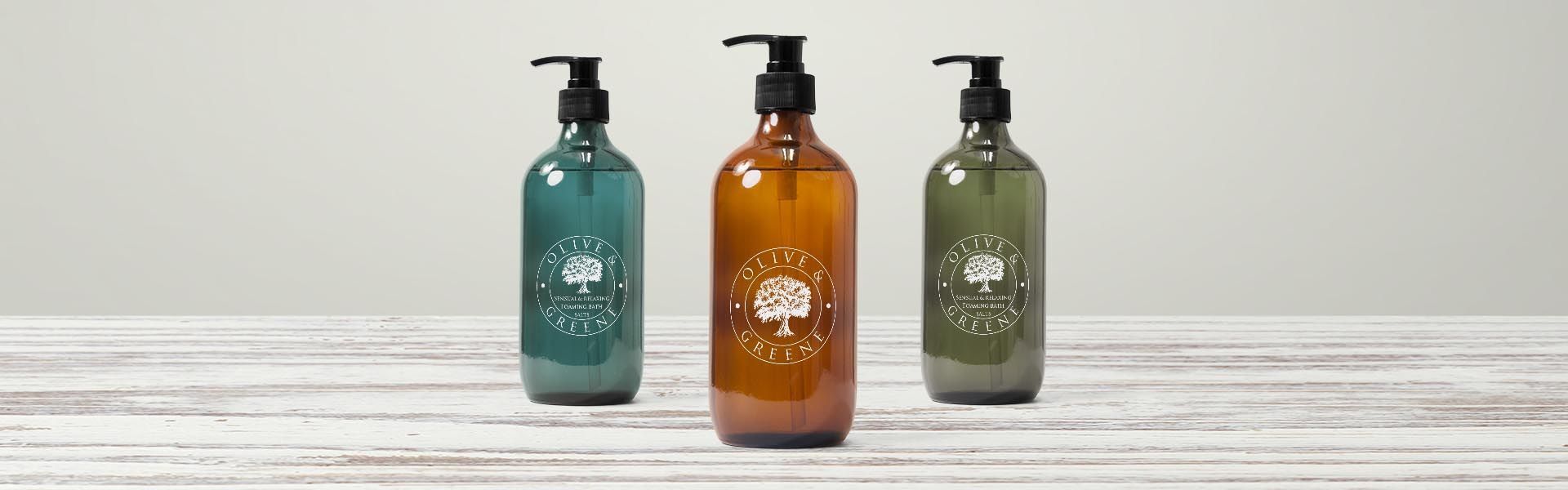 three bottles of olive greene soap sit on a wooden table
