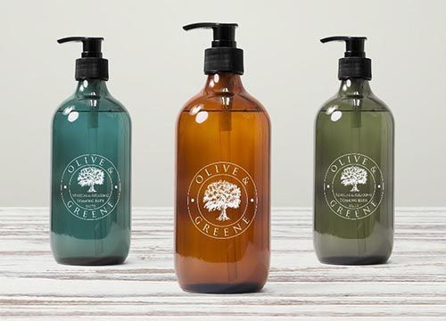 three bottles of olive & greene soap are sitting on a wooden table .