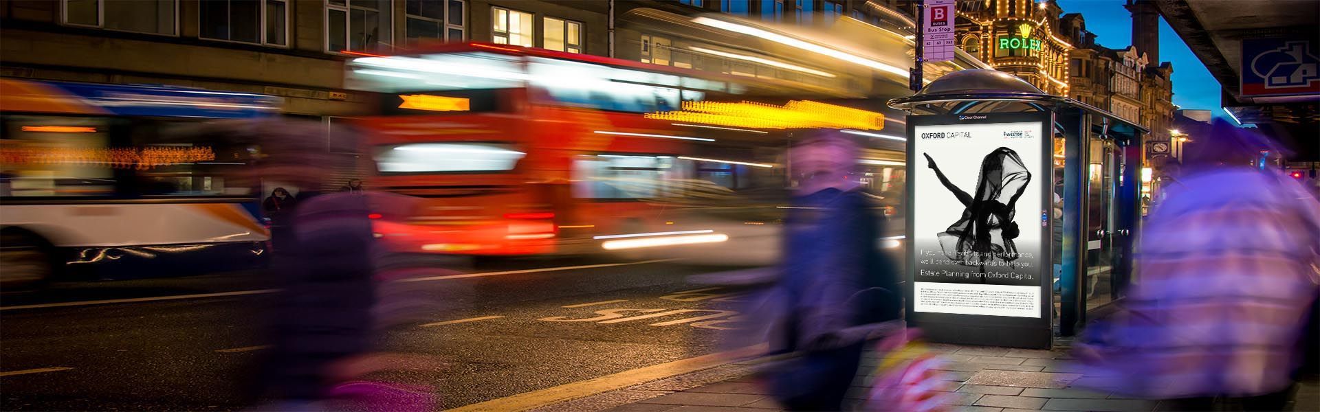 a blurry picture of people walking on a street with an advertising hoarding for oxford capital