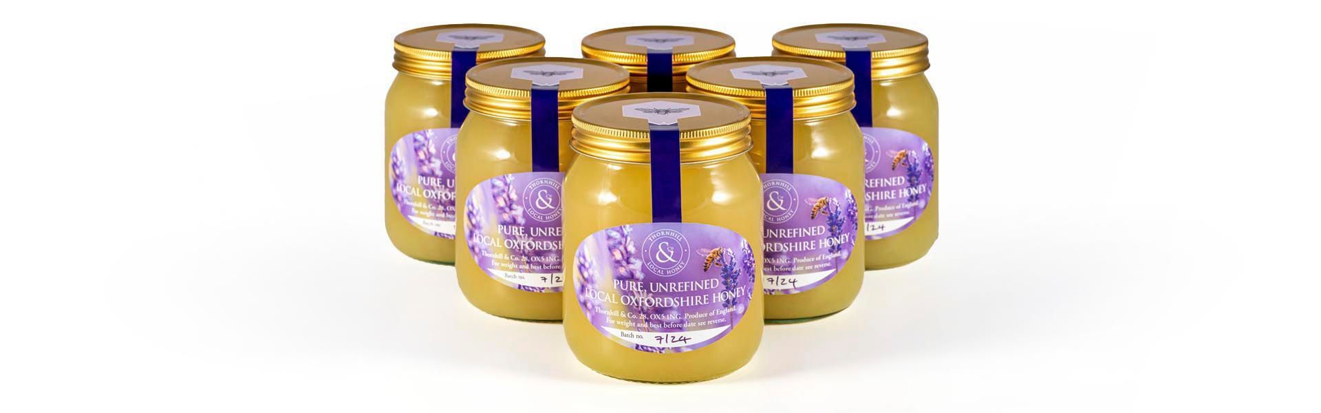 Six jars of honey are stacked on top of a white background.