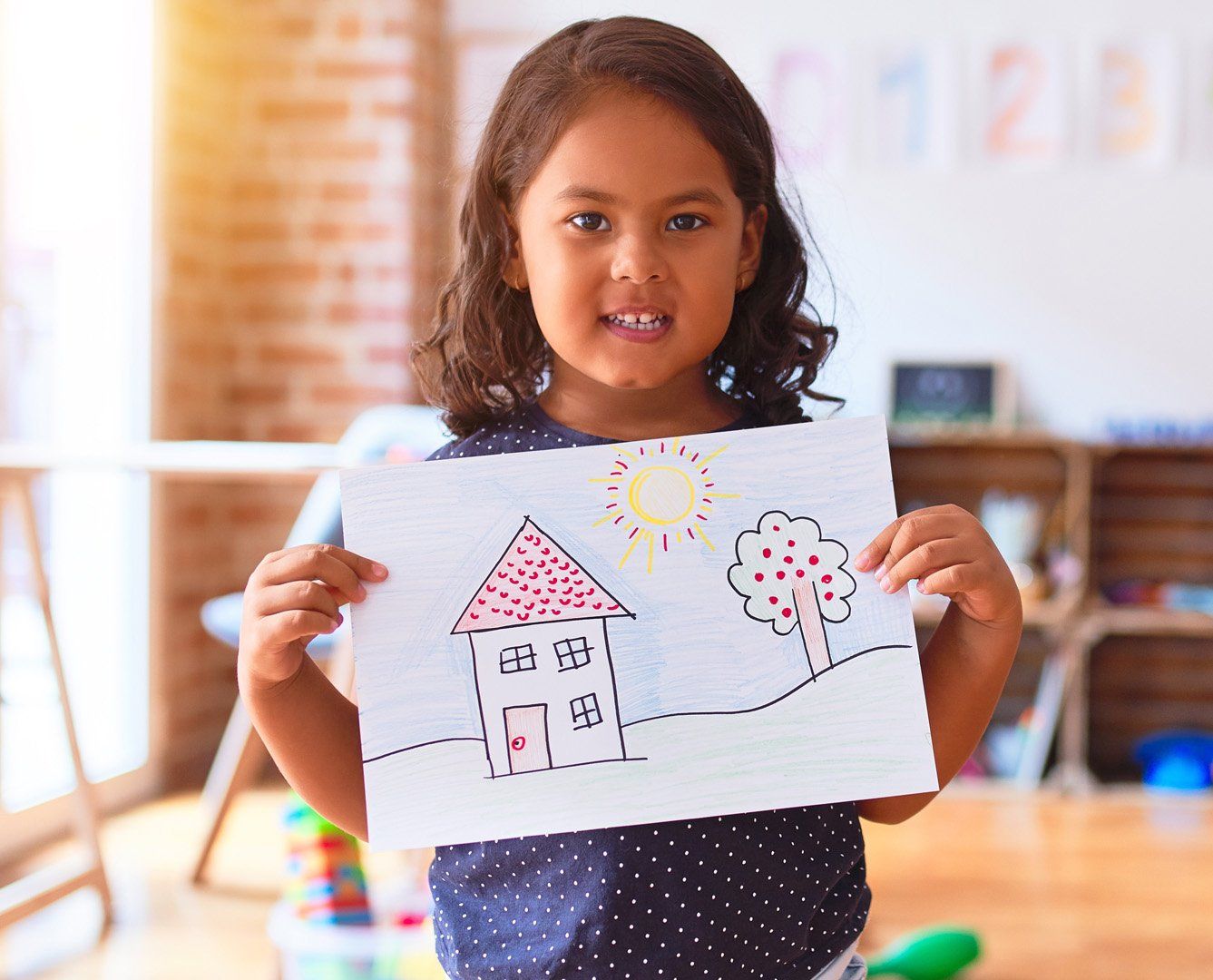 Young girl holding a hand drawn picture of a house on a hill