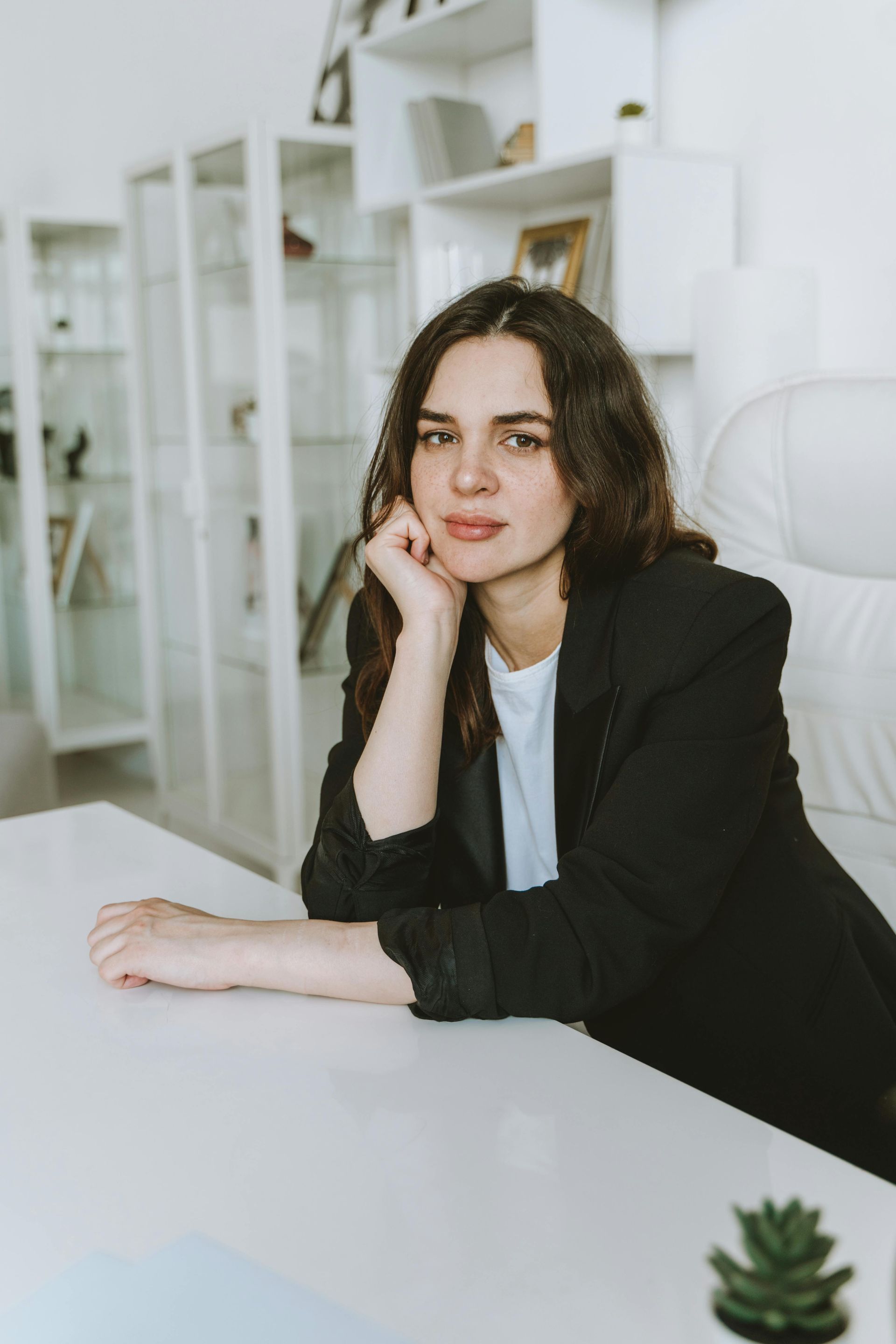A woman is sitting at a desk with her hand on her chin.