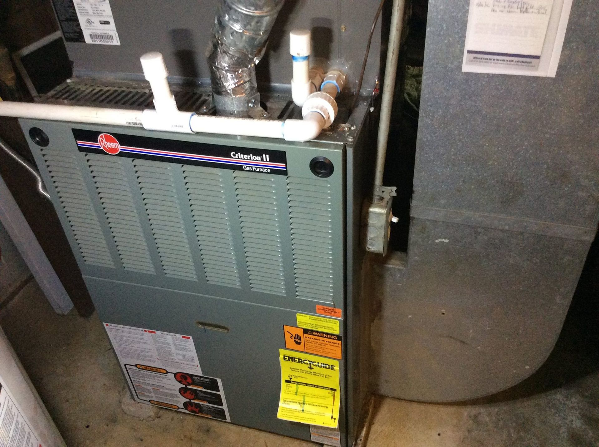 A furnace is sitting in a basement next to a wall.