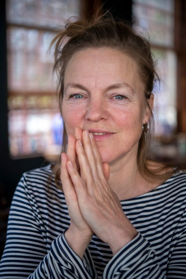 Een vrouw in een gestreept shirt zit aan een tafel met haar handen gevouwen voor haar gezicht.