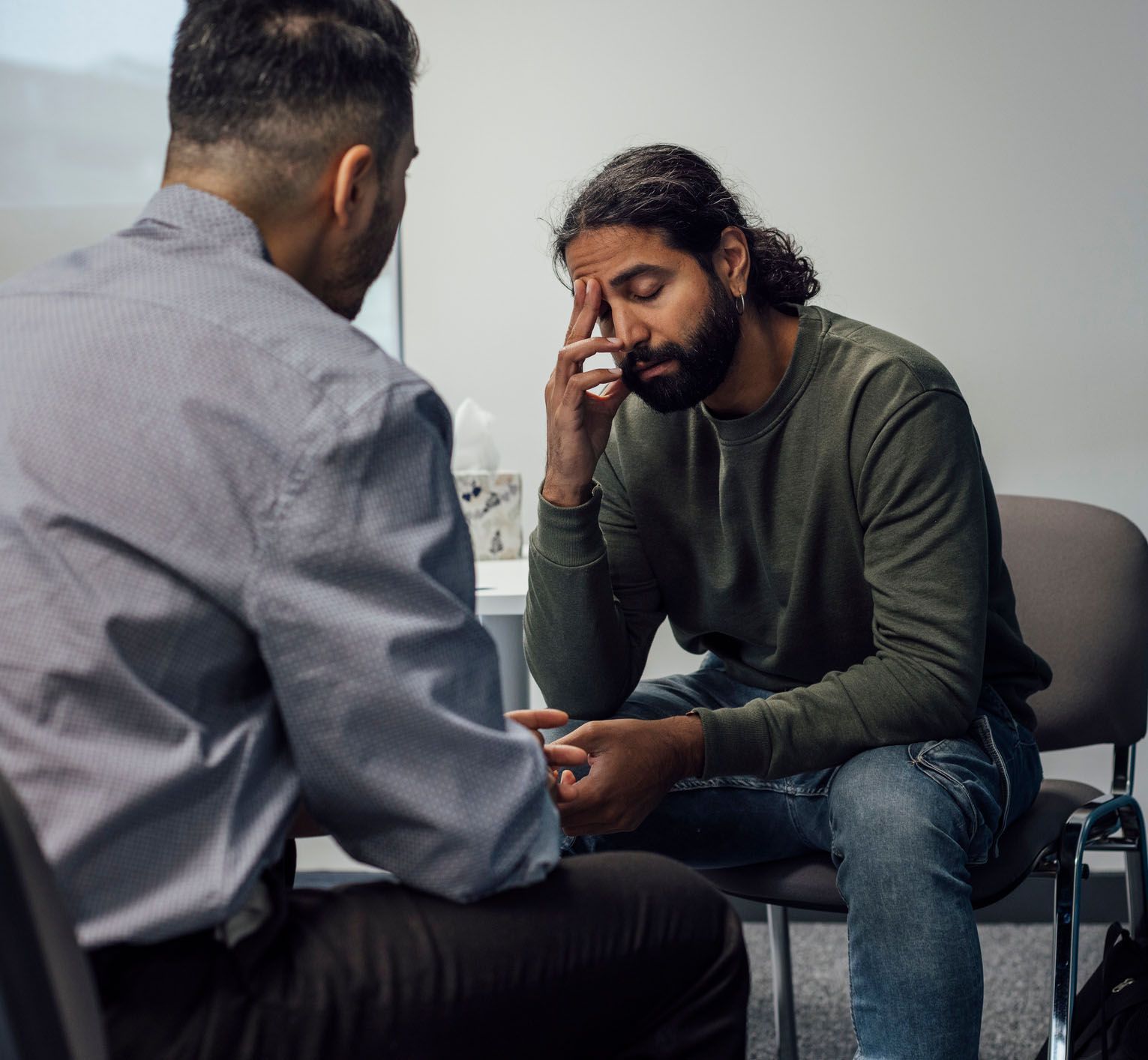 Man with hand on forehead, seated, appears distressed
