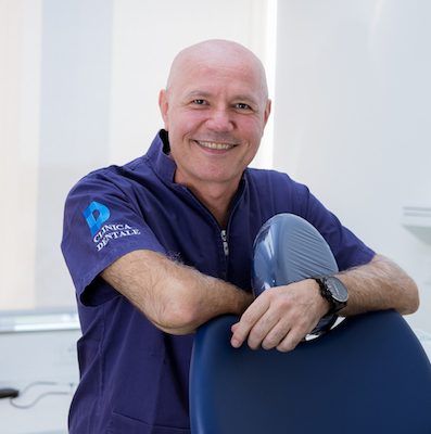 Un uomo con una camicia viola è seduto su una poltrona del dentista e sorride.