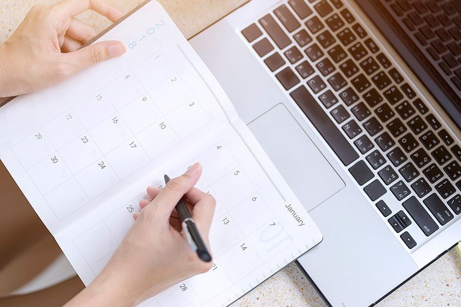 Person using a pen to write in a calendar next to a laptop.