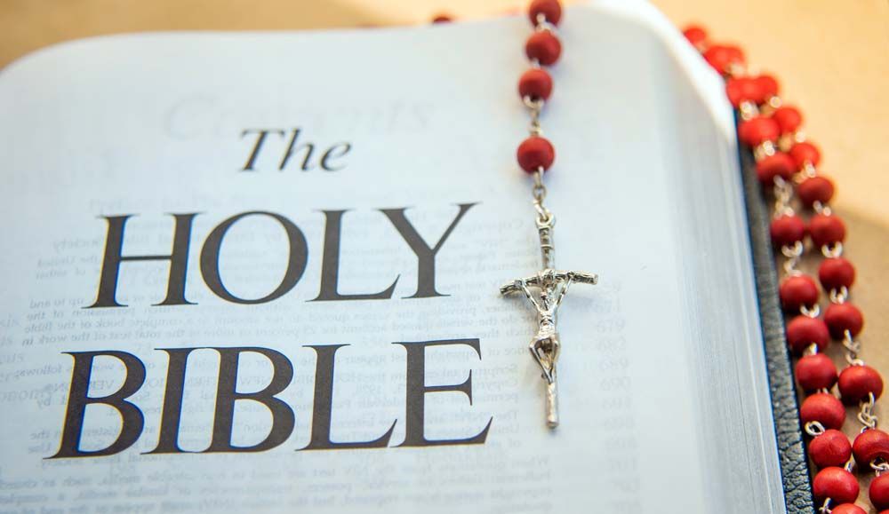 Open Bible with rosary draped across the pages; red beads and silver crucifix.