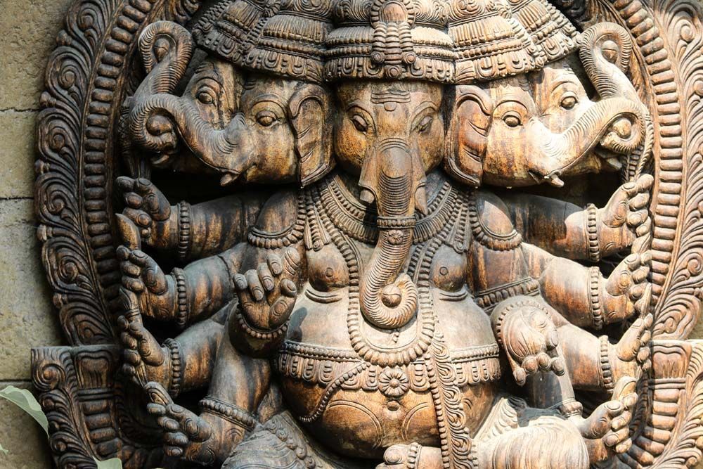 Multi-headed Ganesha carving, detailed wooden statue of the Hindu deity, hands raised, elaborate headdress.