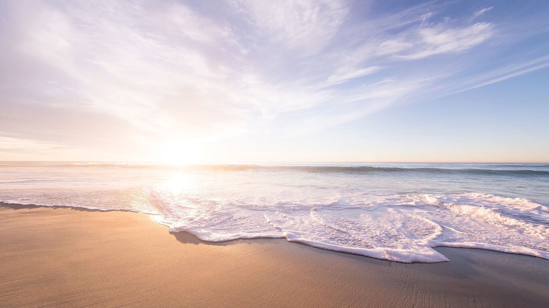 Sandy beach with gentle waves under a bright, sunny sky.