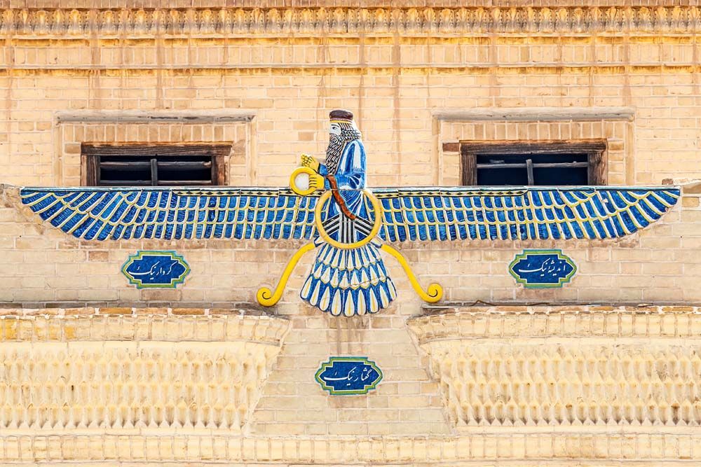 Faravahar emblem in blue and white on a brick wall.
