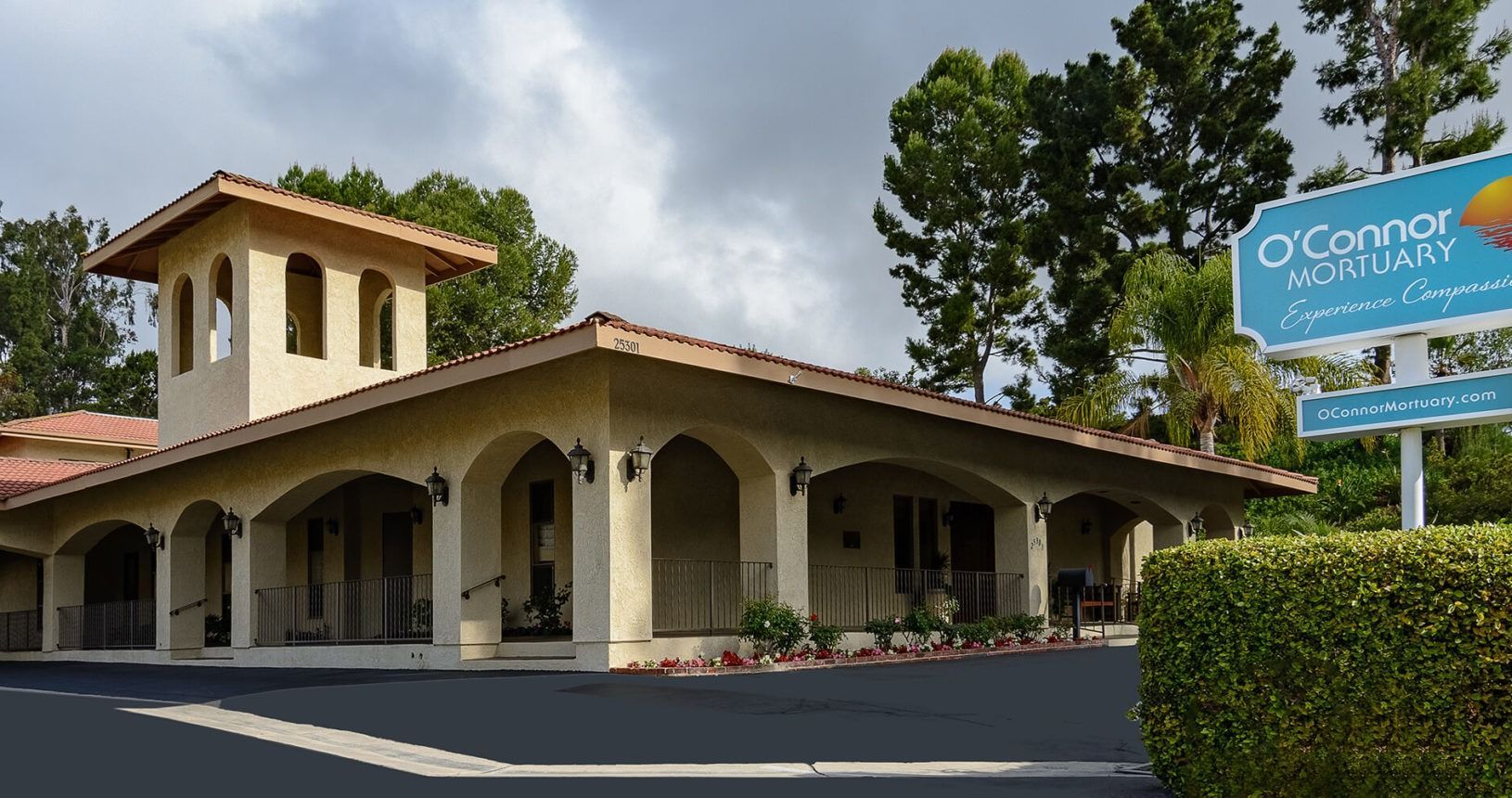O'Connor Mortuary building with sign, beige stucco exterior, tiled roof, archways, and a cloudy sky.