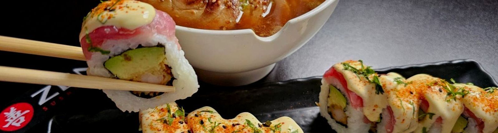 Una persona sostiene un trozo de sushi con palillos al lado de un tazón de sushi.
