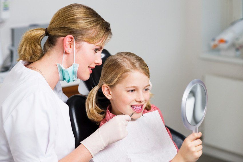 child holding a mirror to look at her teeth at the dentists