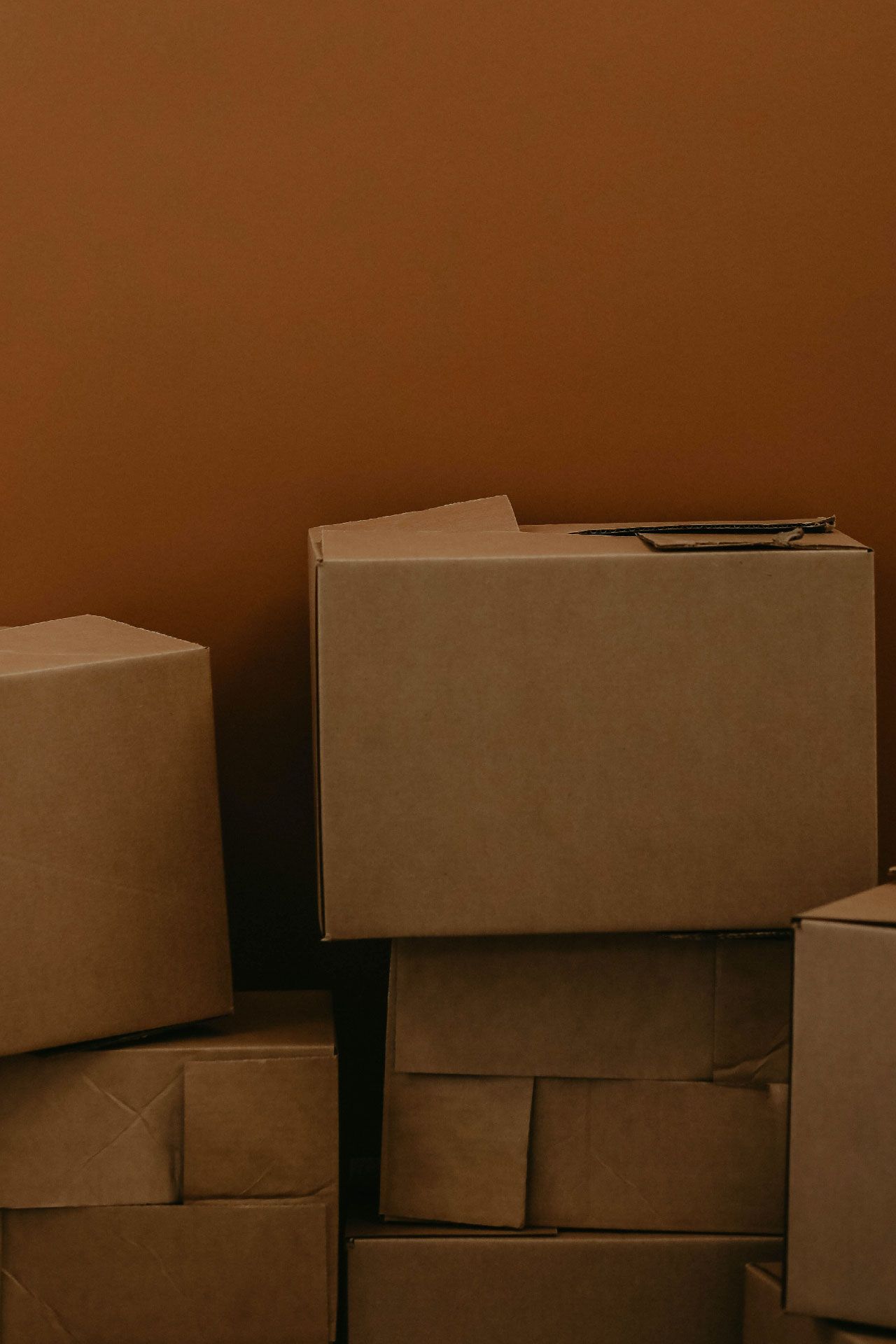 Cajas de cartón para mudanzas apiladas frente a una pared marrón sólida.
