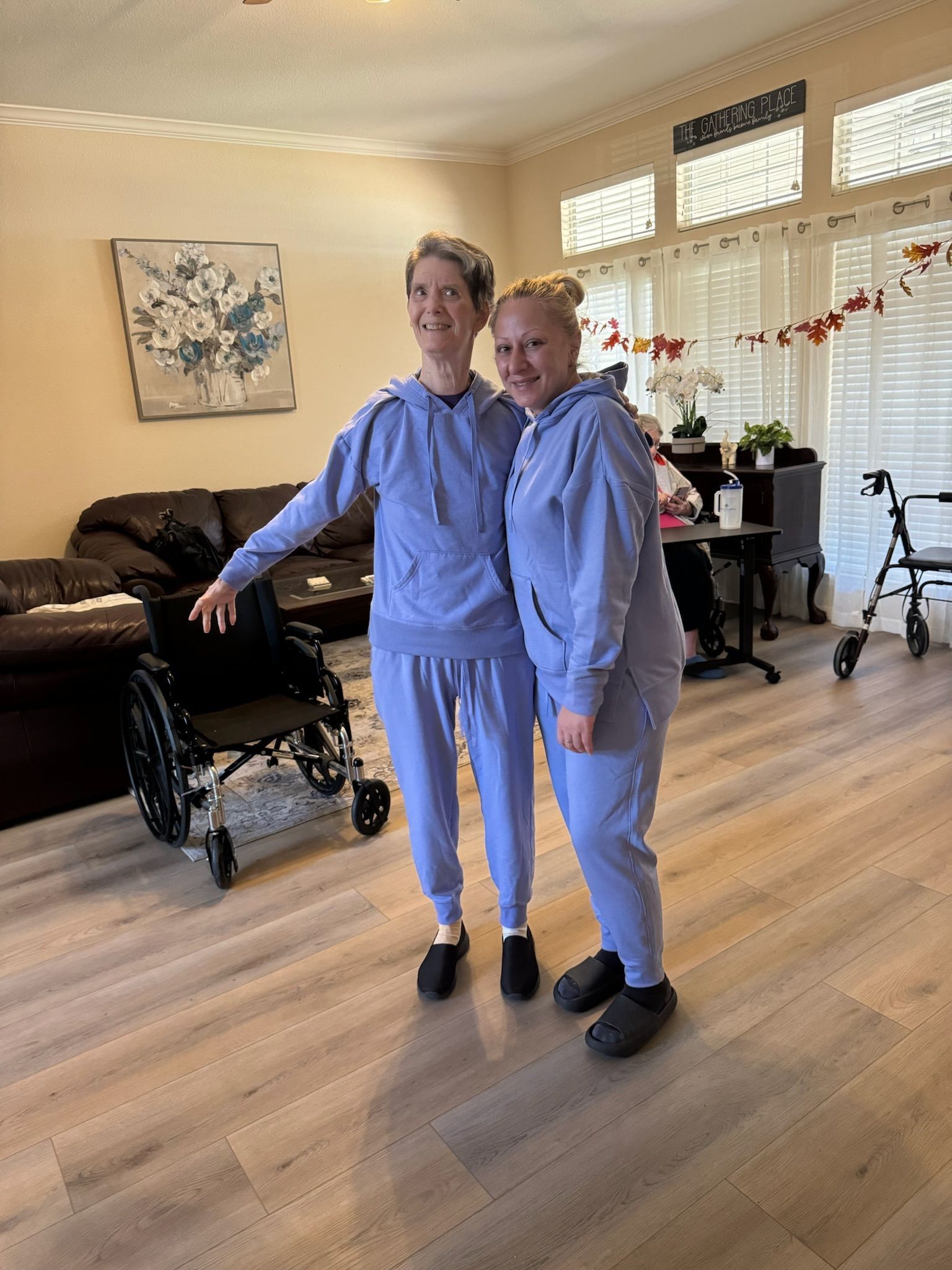 Two women are standing next to each other in a living room in front of a wheelchair.