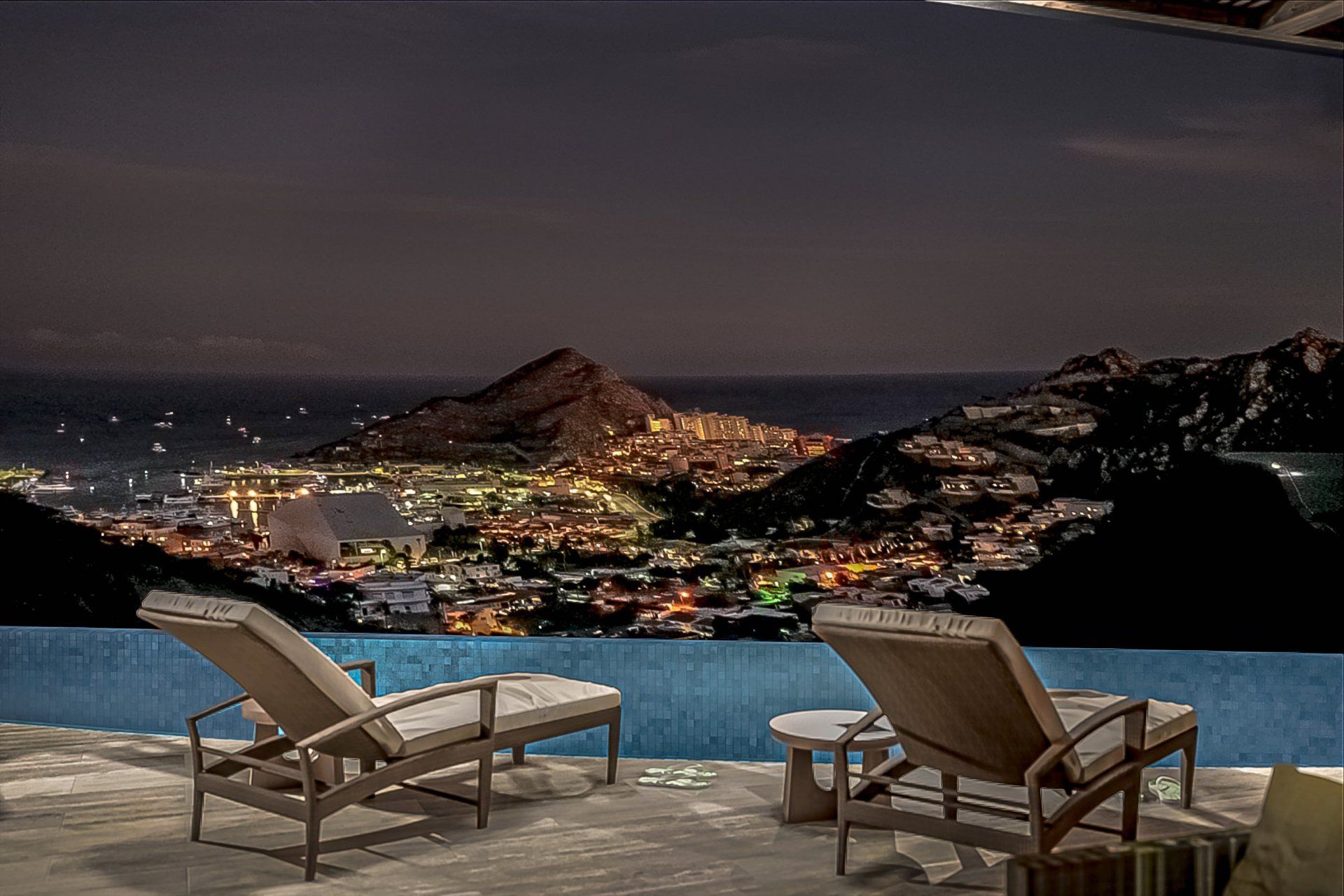 A swimming pool with chairs and a view of a city at night.