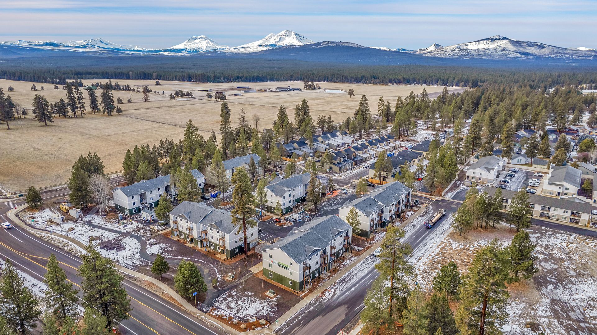 An aerial view of a residential area with snow on the ground and mountains in the background.