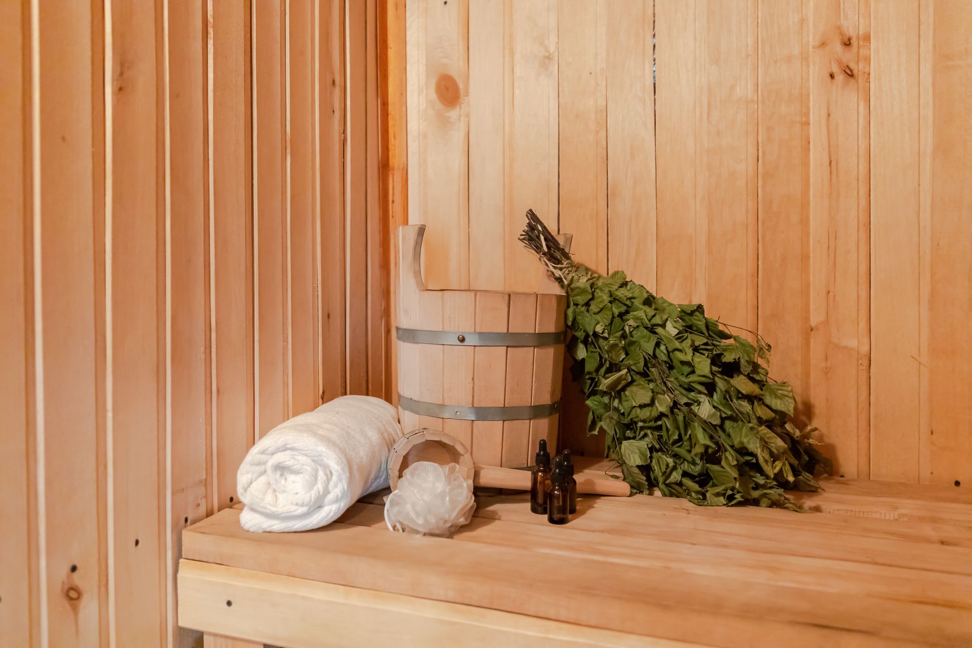 A wooden sauna with a towel , bucket , and broom on the bench.