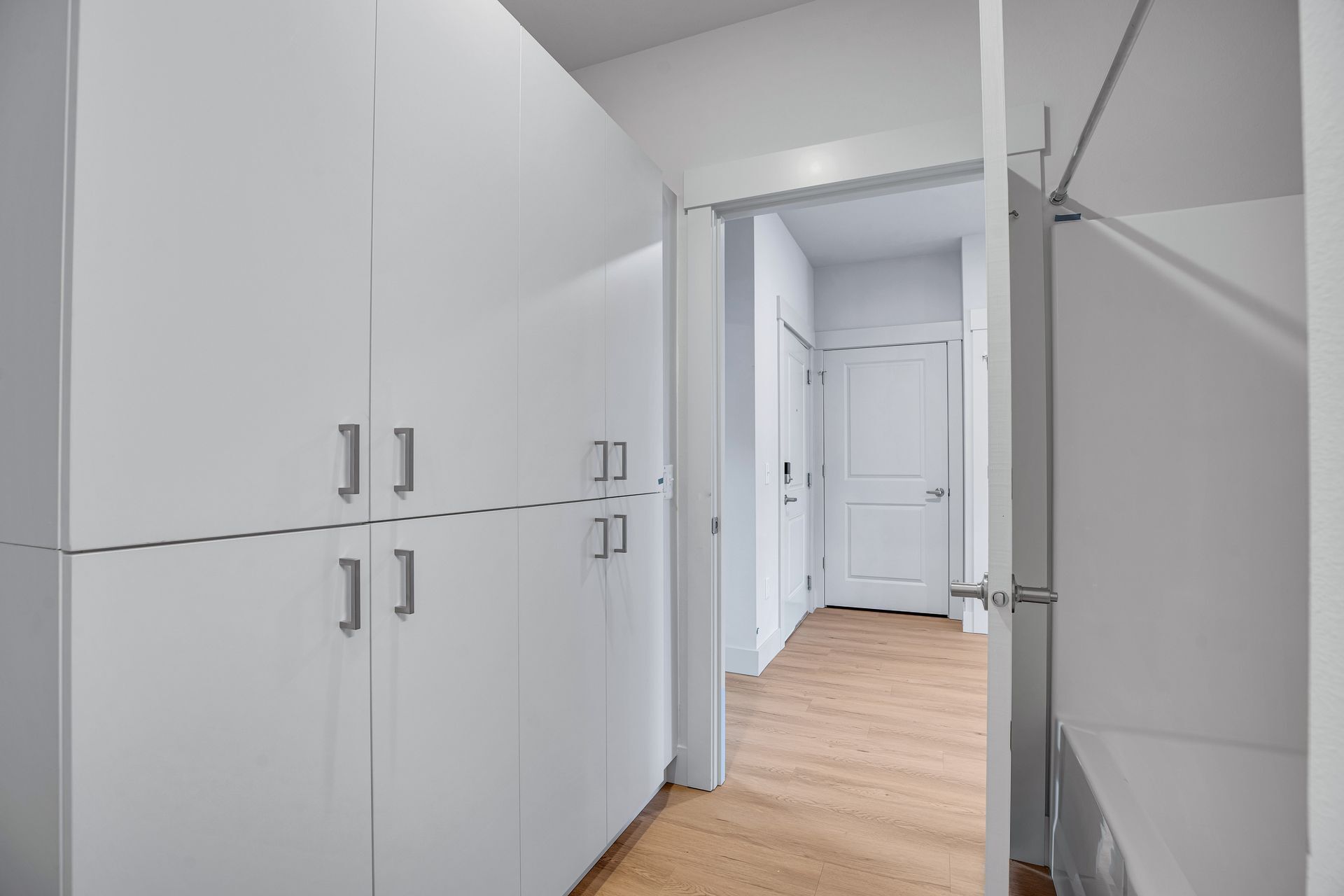 A hallway with white cabinets and wooden floors leading to a door.