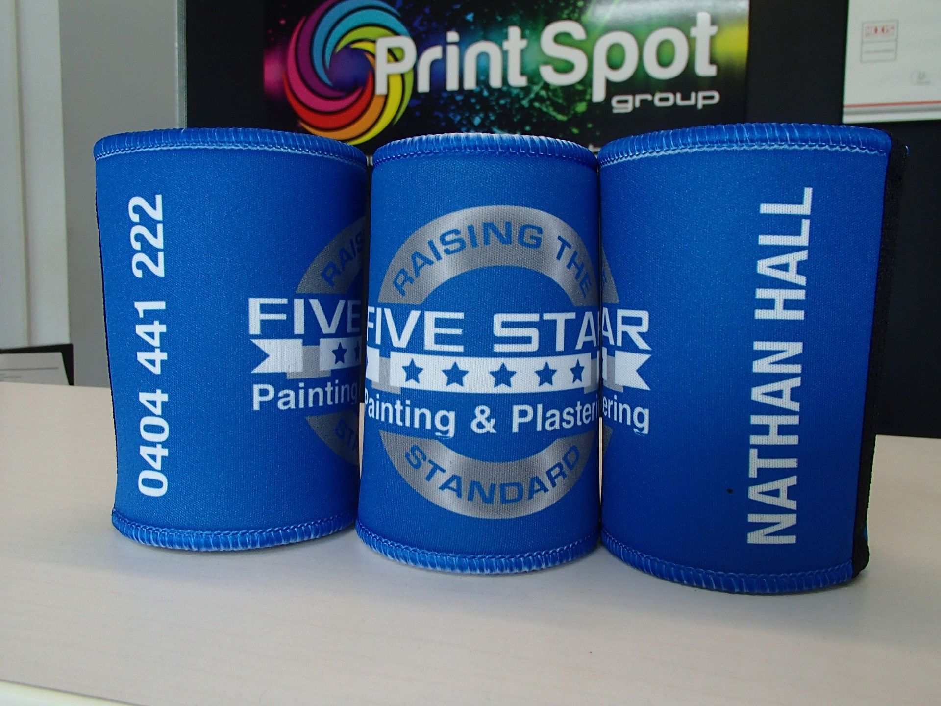 Three blue can coolers, with white text for a painting company, phone number, and individual name.