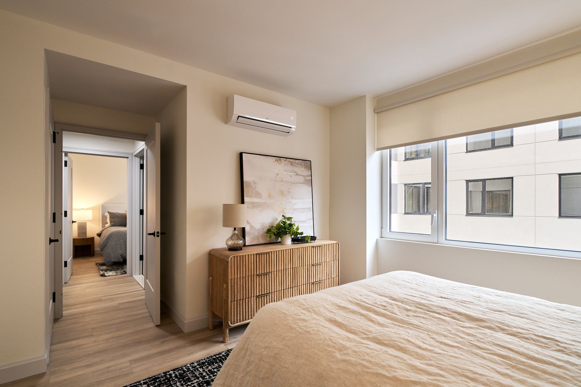 A bedroom with a bed , dresser , window and air conditioner.
