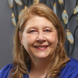 A woman wearing a blue shirt and earrings is smiling for the camera.