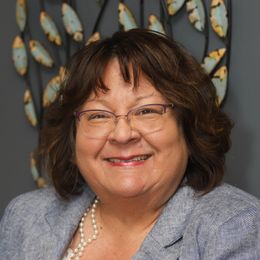 A woman wearing glasses and a pearl necklace is smiling for the camera.