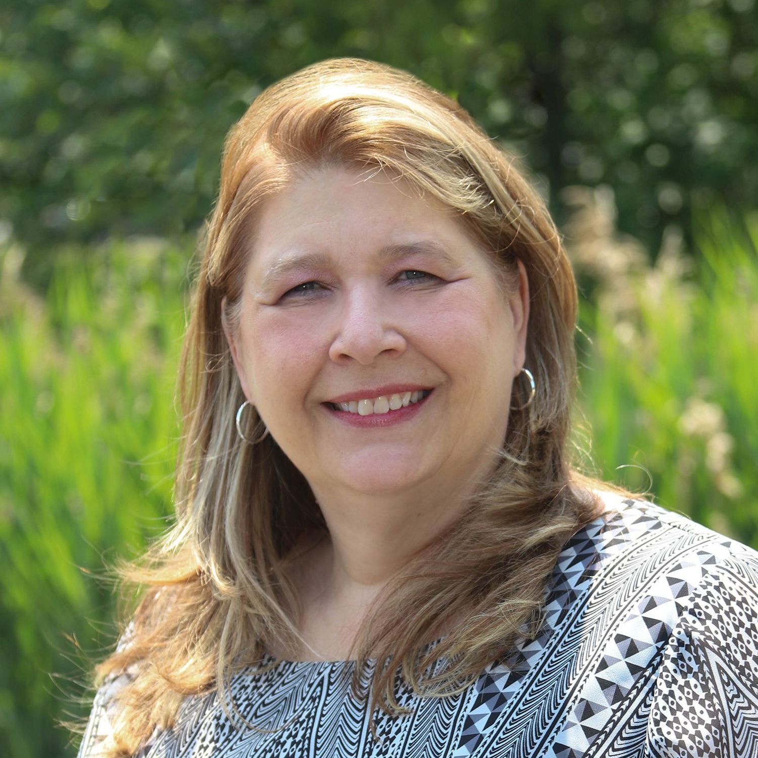 A woman is smiling for the camera in front of a field of tall grass.