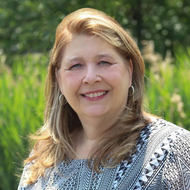 A woman is smiling for the camera in front of a field of tall grass.