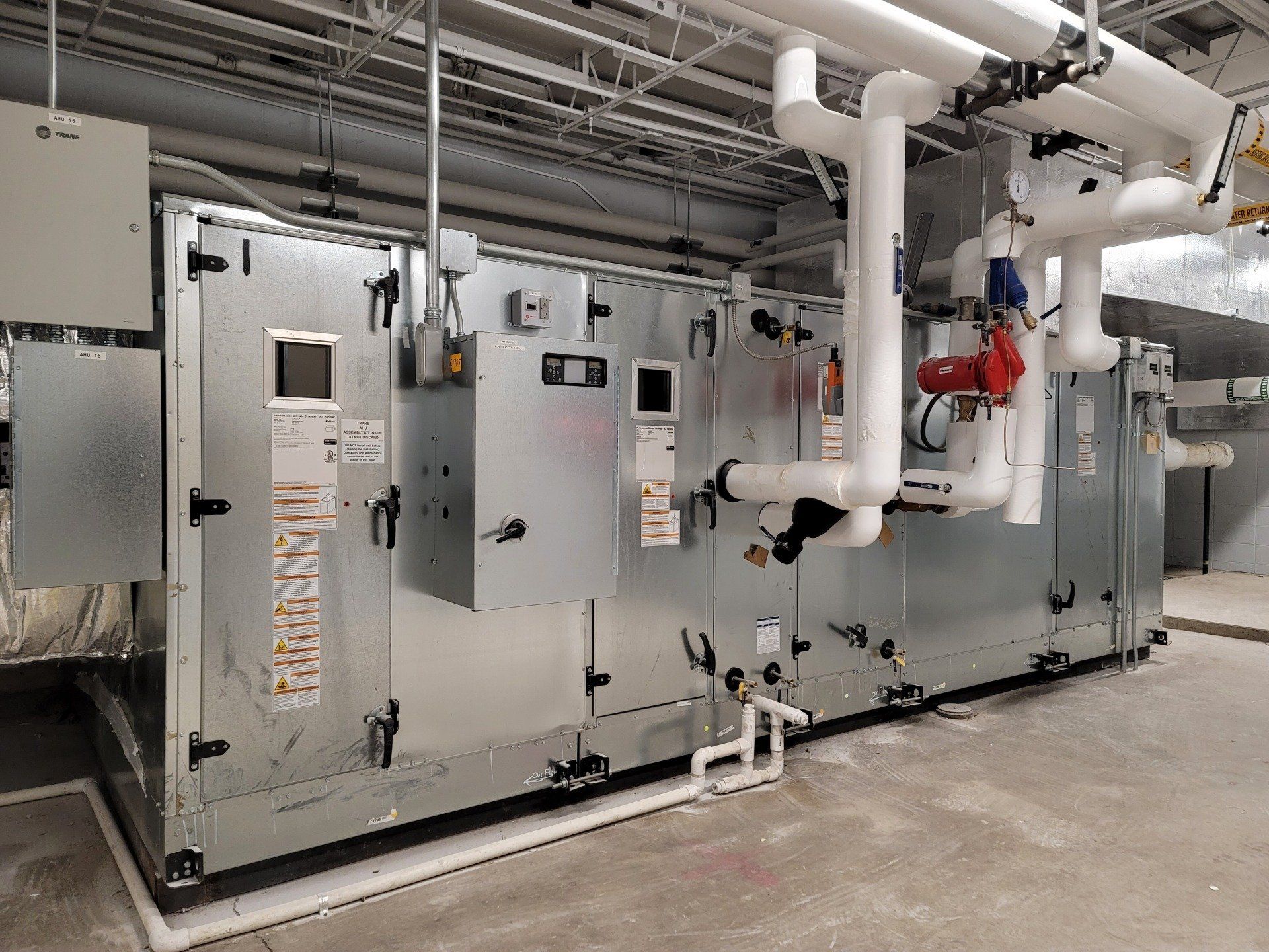 A large machine is sitting in a room with pipes hanging from the ceiling.