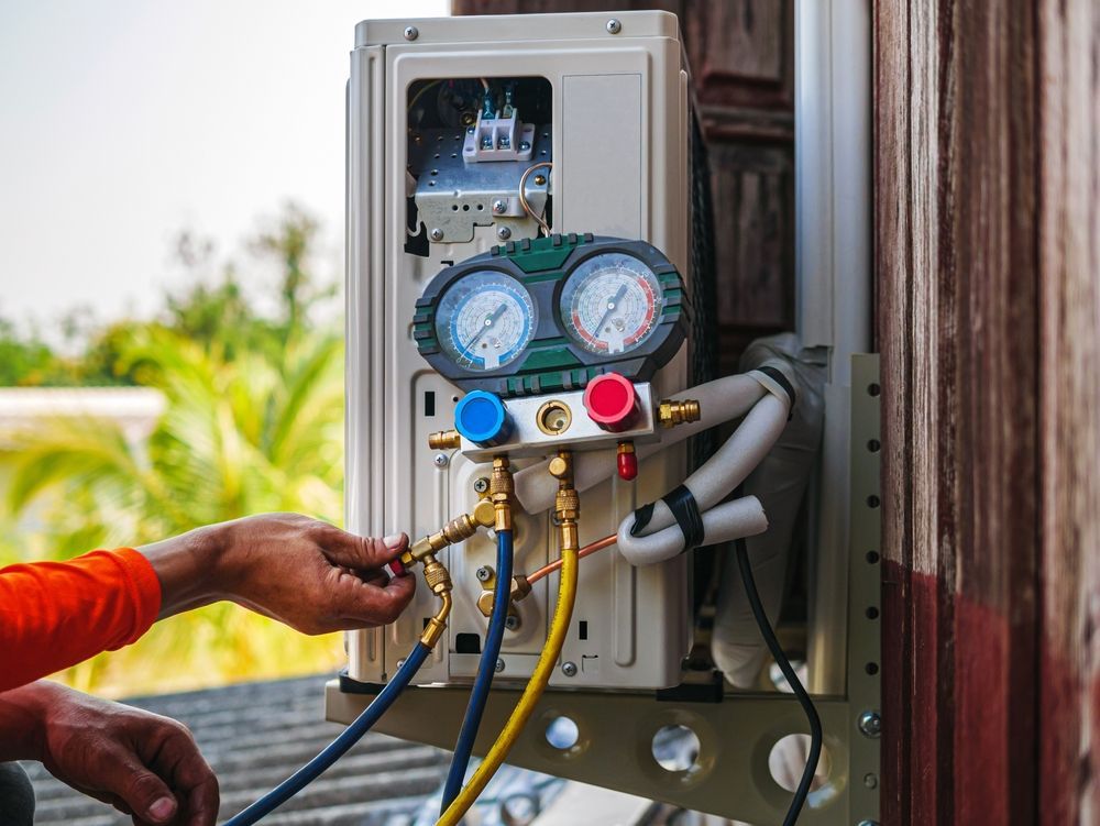 A person servicing an air conditioner unit, attaching gauges with hoses.