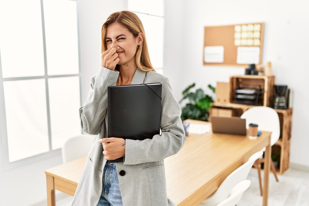 A woman is holding a folder and covering her nose in an office.