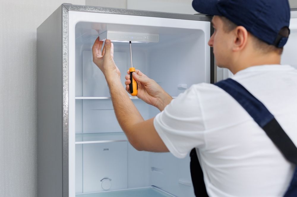 A man is fixing a refrigerator with a screwdriver.