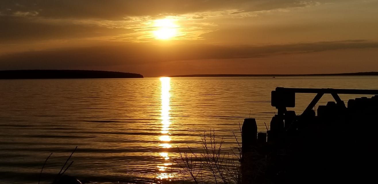 A golden sunset over a calm lake, with a silhouetted wooden pier visible in the foreground.
