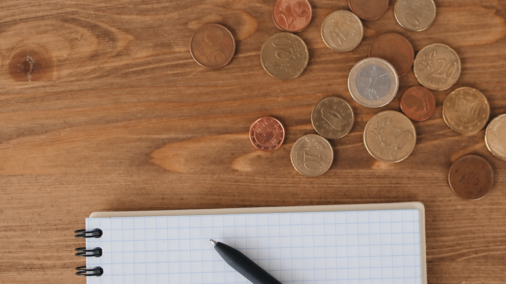 A notebook with a pen and coins on a wooden table.