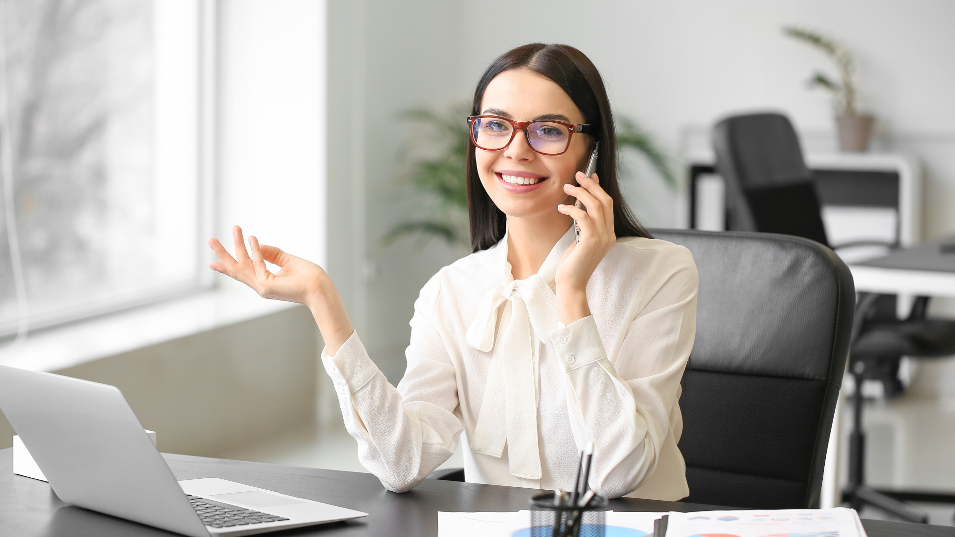 A woman is sitting at a desk talking on a cell phone.