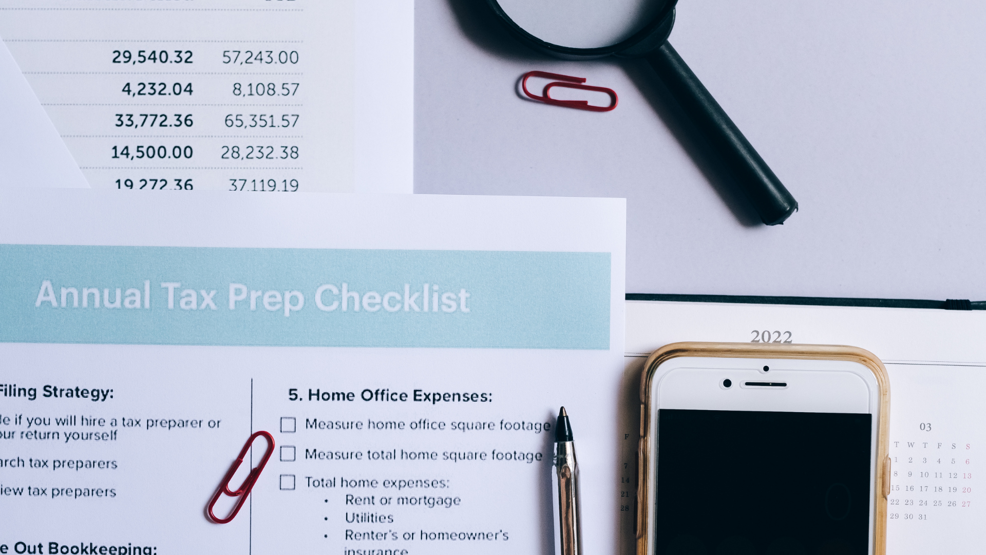 An annual tax prep checklist is sitting on a table next to a cell phone and a magnifying glass.