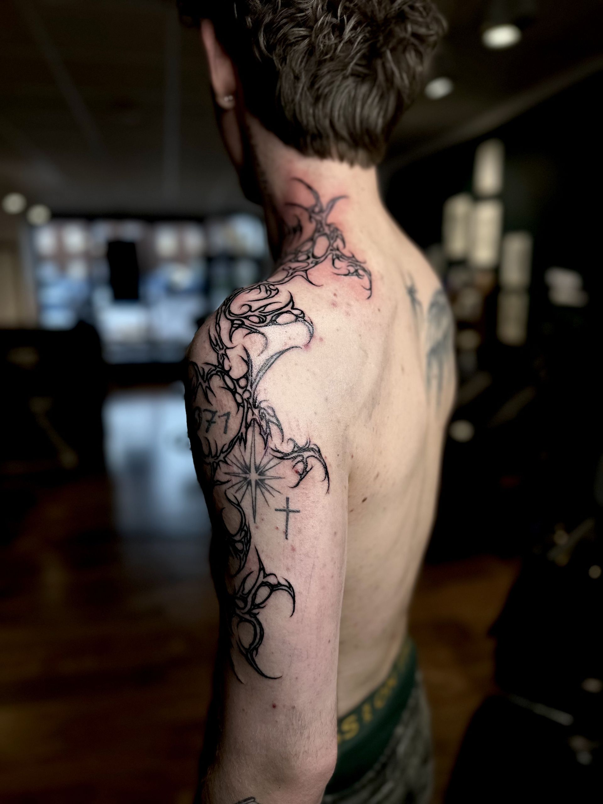 A person viewed from behind with a black-ink, tribal-style ornamental tattoo covering their right shoulder and neck.