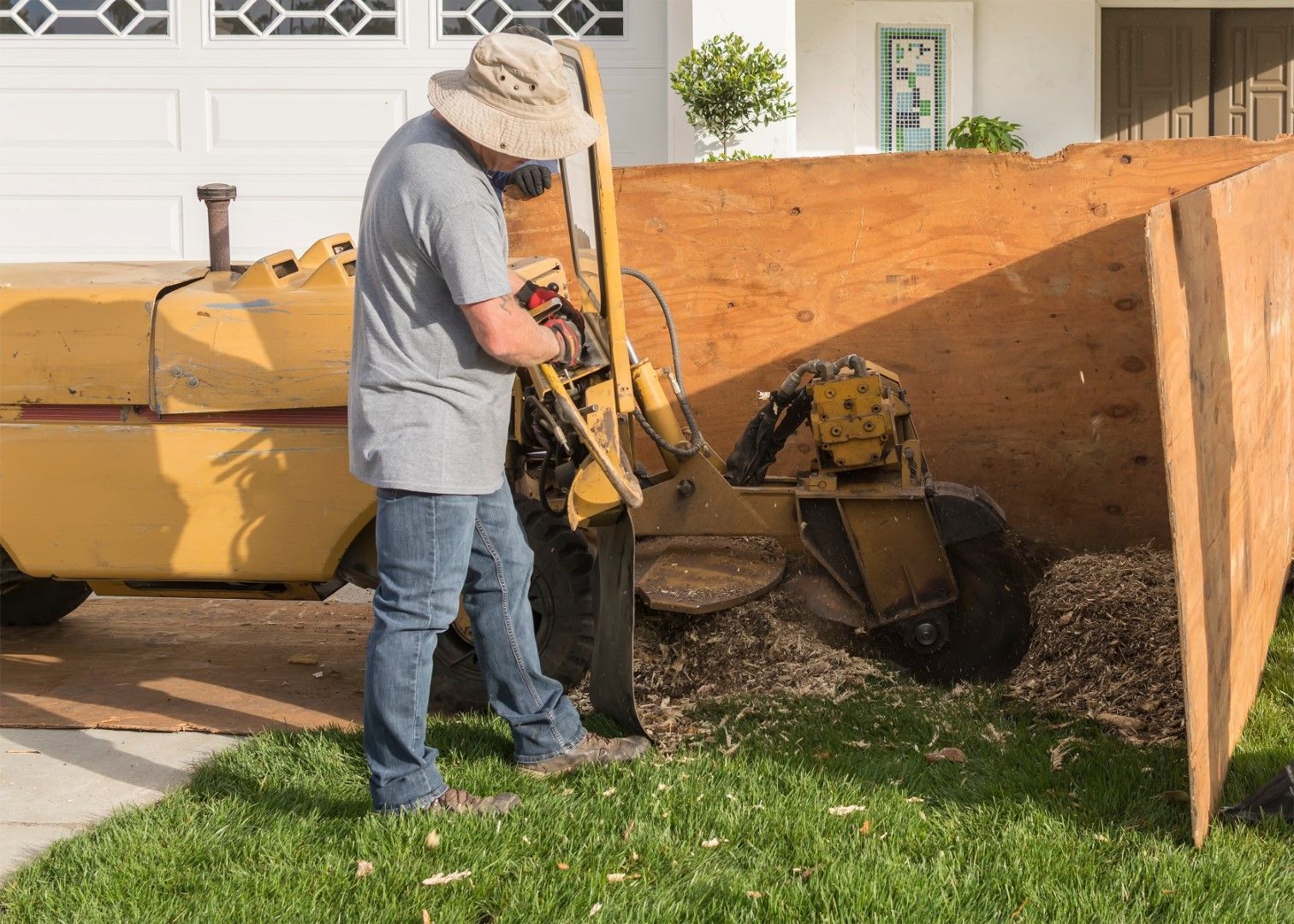 Operator using a walk-behind stump grinder on a residential lawn.